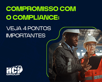 A imagem apresenta dois profissionais dentro de uma indústria dialogando. Os dois estão com uniformizados e equipados de capacete e óculos de segurança.